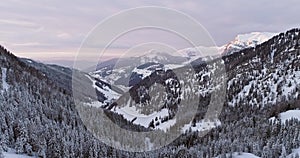 Backward aerial to snowy valley with woods forest at Sella pass.Sunset or sunrise,cloudy sky.Winter Dolomites Italian