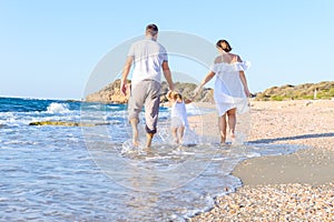 Backward Happy family of three - mother, father and daughter holding hands and having fun walking on the beach. Family vacation, t