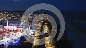 backwards aerial footage of the Carolina Beach Boardwalk with a Ferris wheel, colorful amusement rides, people walking