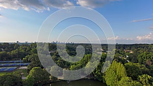 backwards aerial footage a gorgeous summer landscape at Piedmont Park with Lake Clara Meer, lush green trees, buildings, blue sky