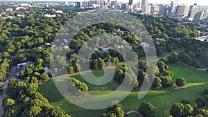 backwards aerial footage of a gorgeous summer landscape at Piedmont Park with lush green trees, grass and plants, homes and people