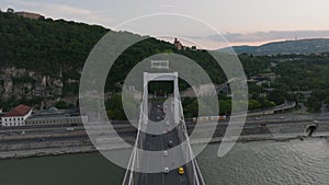 Backwards reveal of Erzsebet Bridge over wide Danube river at twilight. Vehicles driving along river and on bridge