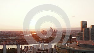 Backwards reveal of top of Arena Tower building. Panoramic view of city with skyline against sunset sky. London, UK