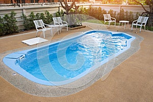 Backyard area with swimming pool blue water and tables chairs and trees fenced background , swimming pool garden