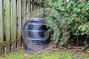 Backyard composter next to a fence and hedge