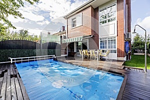 Backyard of a detached house with French windows, with swimming pool covered by a blue protective tarp, acacia wood floors, metal