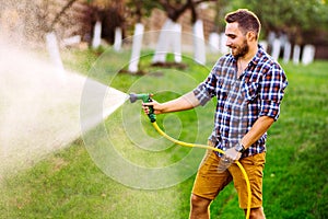 Backyard gardening details - portrait of gardener using water hose and watering the lawn, grass and plants