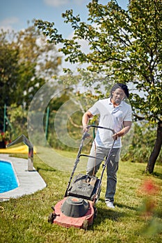 Backyard Oasis: Man Tending to the Lawn Beside the Pool