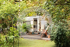 Backyard with RV house with garden furniture. Two deckchairs near outside caravan trailer.