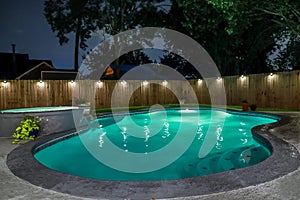 A backyard swimming pool and jacuzzi hot tob at night