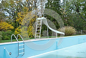Backyard swimming pool with pool slide and ladder emptied out shutting down for winter