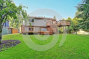 Backyard view of grey rambler house with upper and lower decks