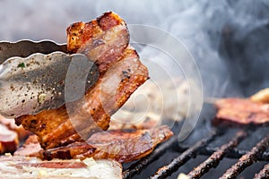 Bacon barbecue in metal tongs close up