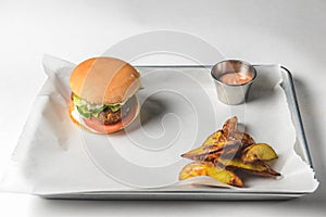 Bacon burger with beef patty, fresh tomatoes and cucumbers with sauce served on a metal tray over white background