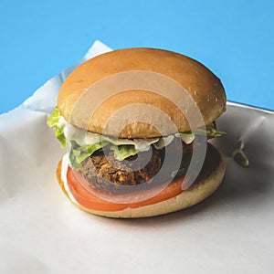 Bacon burger with beef patty, fresh tomatoes and cucumbers with sauce served on a metal tray over white background