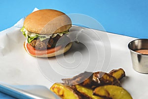 Bacon burger with beef patty, fresh tomatoes and cucumbers with sauce served on a metal tray over white background