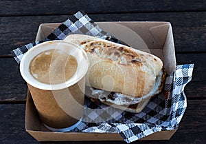 Bacon and egg breakfast ciabatta roll with take away coffee with checkered serviettes in box