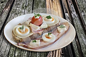 Bacon And Egg Sandwich With An Extra Belly Bacon Rasher Served On Porcelain Plate Set On Old Cracked Pine Wood Picnic Table