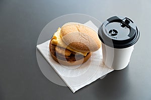 Bacon and Omelette Hamburger on the paper with White paper coffee mug on the table in fast food restaurant