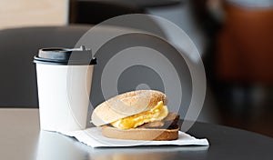 Bacon and Omelette Hamburger on the paper with White paper coffee mug on the table in fast food restaurant