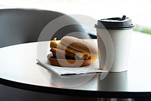 Bacon and Omelette Hamburger on the paper with White paper coffee mug on the table in fast food restaurant