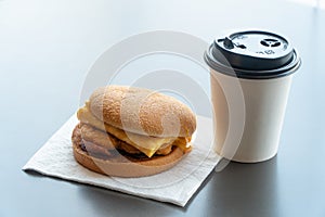 Bacon and Omelette Hamburger on the paper with White paper coffee mug on the table in fast food restaurant