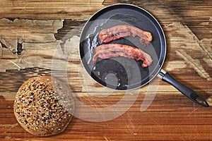 Fried Bacon Rashers In Teflon Frying Pan With Integral Brown Bread Loaf Set On Old Cracked Flaky Wooden Picnic Table photo