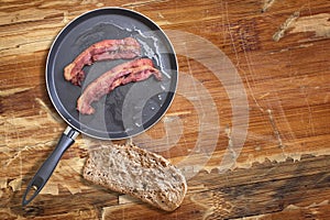 Fried Pork Ham Rashers In Teflon Frying Pan With Slice Of Brown Bread Set On Old Cracked Wooden Picnic Table photo
