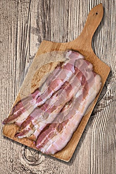 Bacon Rashers On Wooden Cutting Board Set On Old Knotted Rough Pine Wood Table Surface