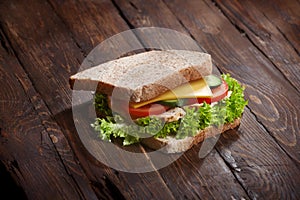 Bacon sandwich closeup with fresh tomatoes, lettuce salad leaves, cucumber and cheese, on wooden rustic table background