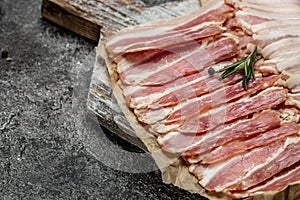Bacon slices and rosemary on a wooden board, Keto diet food ingredients. Food recipe background. Close up