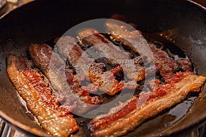 Bacon strips or rashers cooked in frying pan in the rays of sunlight