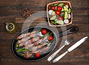 Bacon wrapped asparagus on wooden table.  Cooking asparagus. Food background. Asparagus served on cast-iron frying pan with fresh