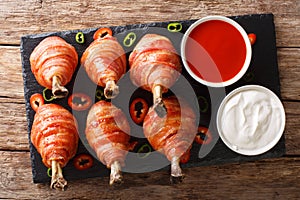 Bacon Wrapped Chicken Lollipops with sauces close-up. Horizontal top view