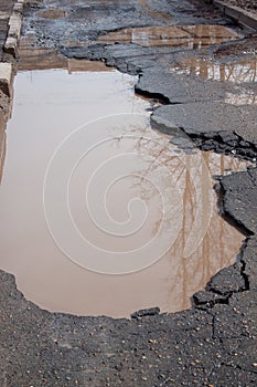 The bad asphalted road. Big pothole filled with water. Dangerous destroyed roadbed.
