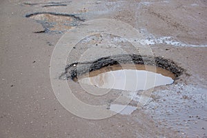 The bad asphalted road with a big pothole filled with water. Dangerous destroyed roadbed.