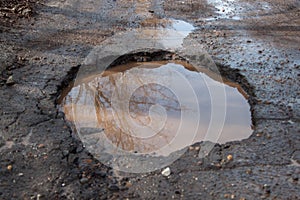 The bad asphalted road with a pothole filled with water. Dangerous destroyed roadbed.