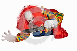 A bad clown lies on the ground and holds a knife in the camera