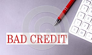 BAD CREDIT text written on a gray background with pen and calculator