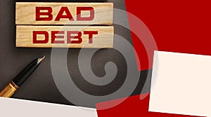 Bad debt on wooden blocks and luxury pen on dark grey background. Financial losses or business bankruptcy Concept