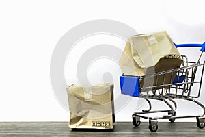 Bad delivery concepts. A damaged container box in small blue shopping cart model and on wood table with white background