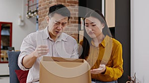 Bad delivery service. Disappointed asian spouses unpacking box, received damaged item, tracking shot, slow motion