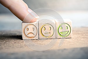 Bad Feedback Concept With Red, Yellow And Green Smiling Faces On Wooden Blocks On A Board, The Red Face Is Touched By A