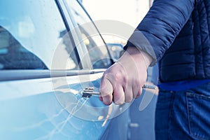 Bad guy scratching the car door with a key in the parking lot on the street. Damage of property from revenge for treason or