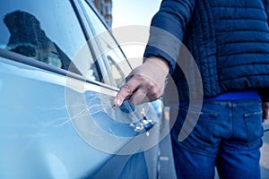 Bad guy scratching the car door with a screwdriver in the parking lot on the street. Damage of property from revenge for treason