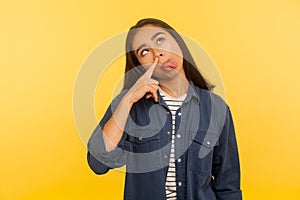 Bad habit, humorous grimace. Portrait of adorable funny girl in denim shirt picking nose and sticking out tongue