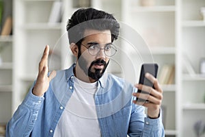 Bad News. Shocked Indian Man Looking At Smartphone In His Hand