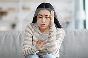 Bad News. Upset Asian Female Holding Smartphone, Looking At Screen With Worry