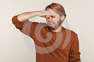 Bad smell. Portrait of bearded man grabbing nose, holding breath and grimacing in disgust, expressing repulsion photo