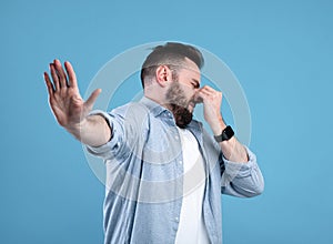 Bad smell. Young bearded guy closing his nose and showing STOP gesture, expressing disgust on blue studio background